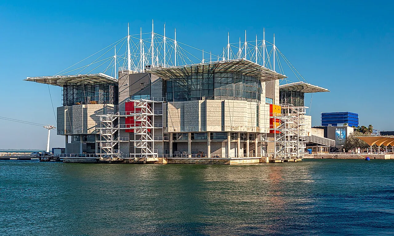 Lisbon Oceanarium building rising from the water on its pier, with its white masts and the river in front