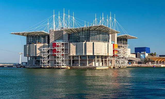 Lisbon Oceanarium building rising from the water on its pier, with its white masts and the river in front
