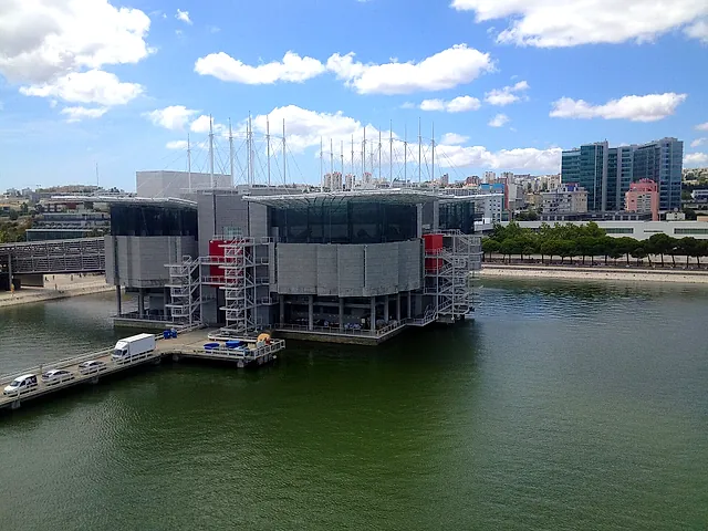 The Lisbon Oceanarium seen from across the water under a blue sky, with Parque das Nações buildings behind