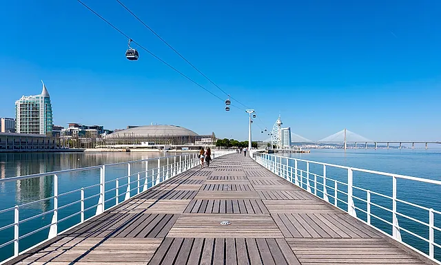 A wooden boardwalk over the water at Parque das Nações with a cable car overhead